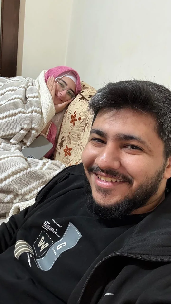Fatima wrapped in a blanket on the sofa, smiling with her cheek in her hand, while I grin at the camera.