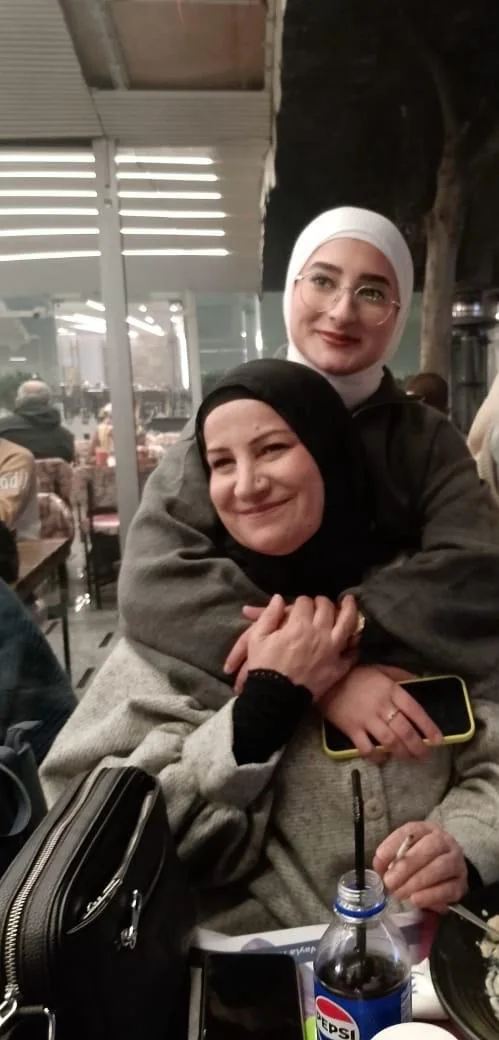Fatima hugging a seated woman from behind at a café, both smiling.