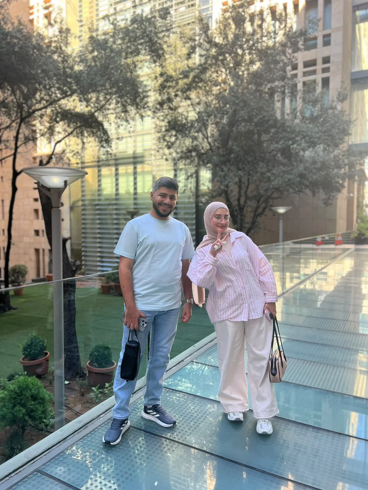 The two of us standing on a glass walkway between tall buildings; Fatima holds up a peace sign.