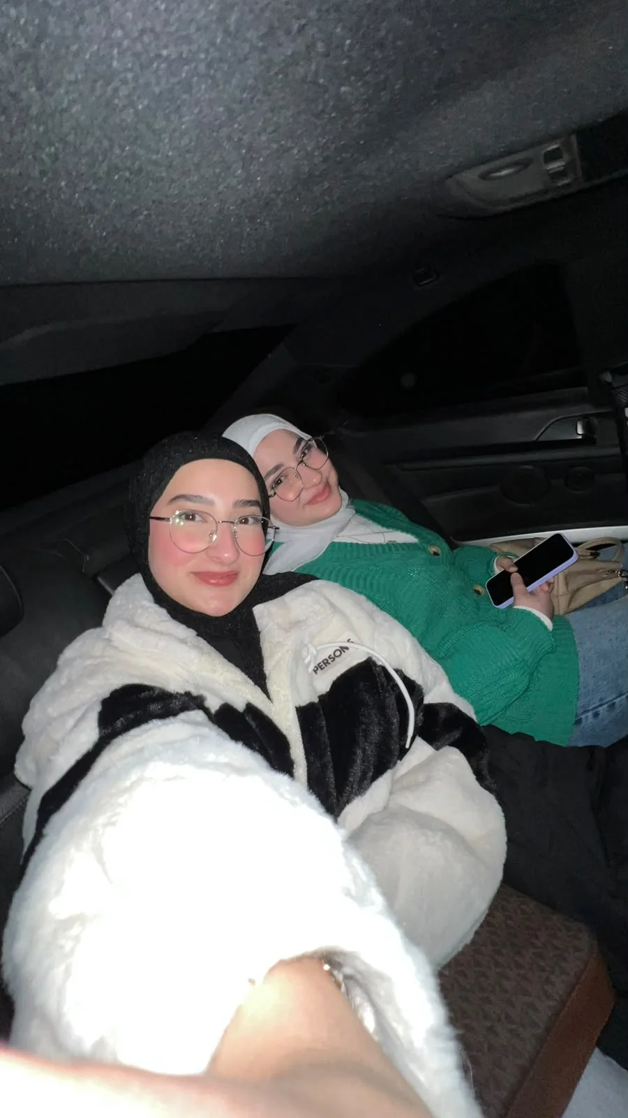A night-time car selfie: two young women in glasses smiling at the camera.
