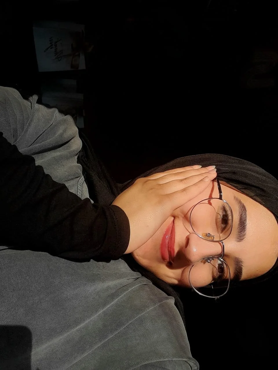 Fatima resting her head on her hand in low light, smiling softly at the camera.