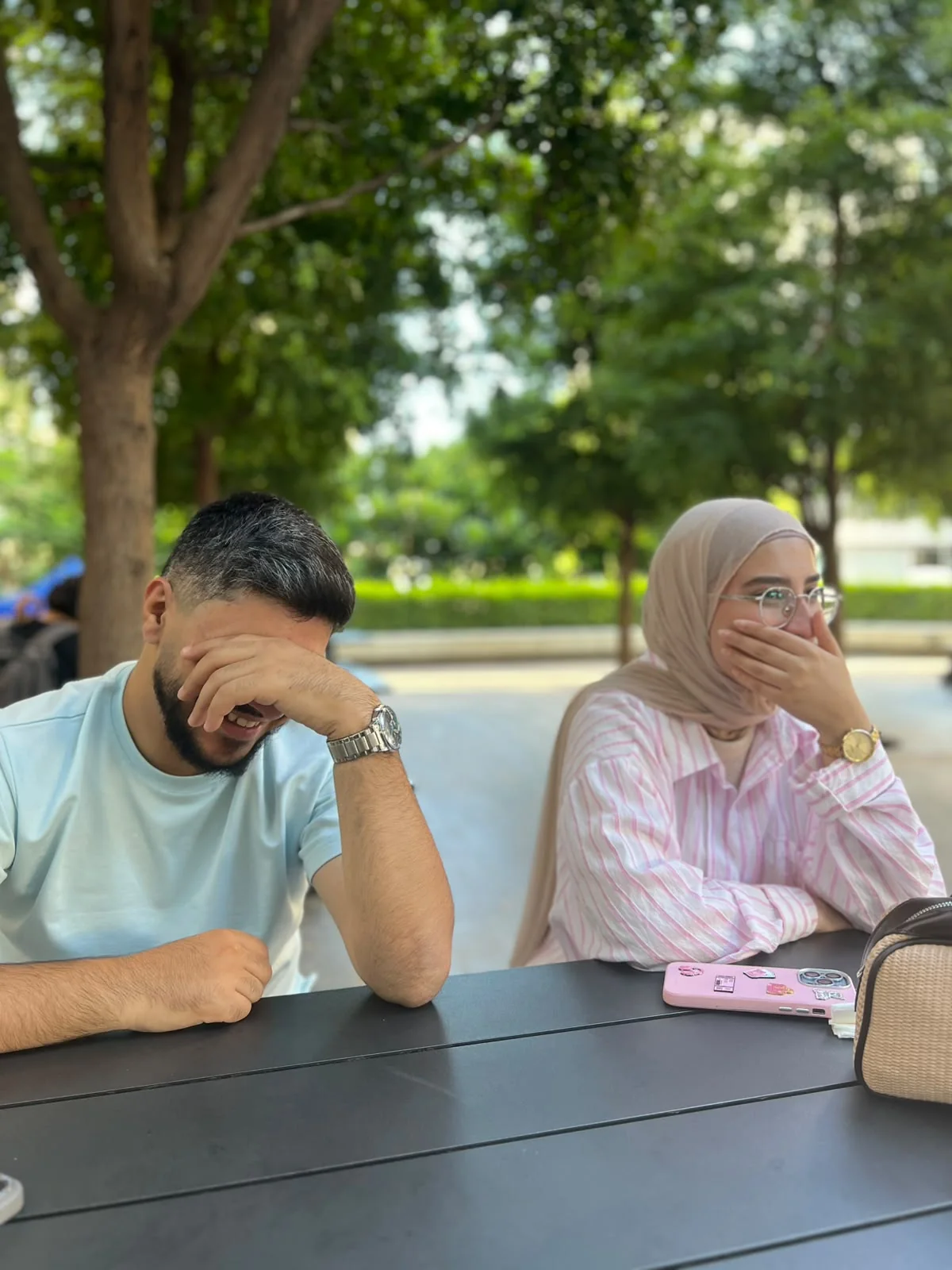 At an outdoor table under the trees, both of us laughing behind our hands.
