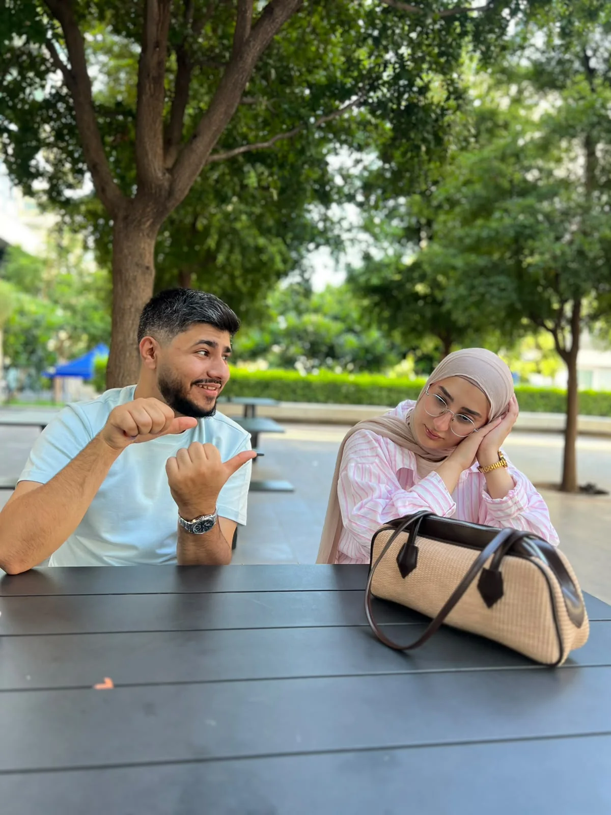 At the same outdoor table: two thumbs pointed her way while Fatima pretends to fall asleep on her hands.